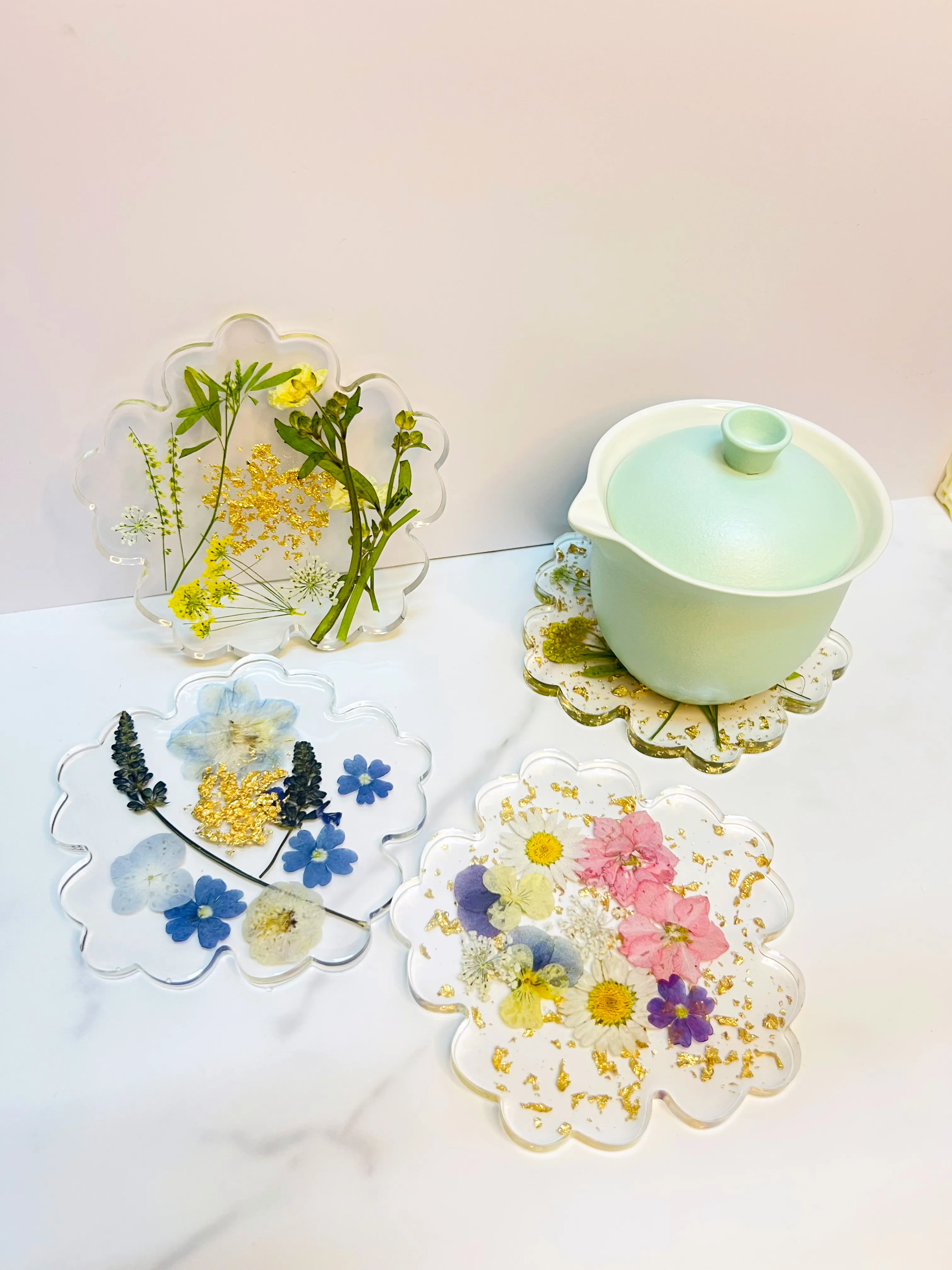 Assorted pressed-flower resin coasters in soft pastels beside a mint teapot, handmade by Jeostyle
